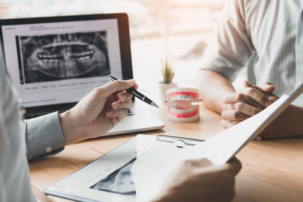Dentiste consultant une radiographie dentaire sur un ordinateur avec un patient lors d'un rendez-vous.