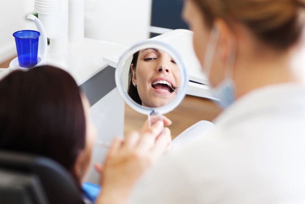 Patient vérifiant ses dents dans un miroir tenu par son dentiste après un soin dentaire.